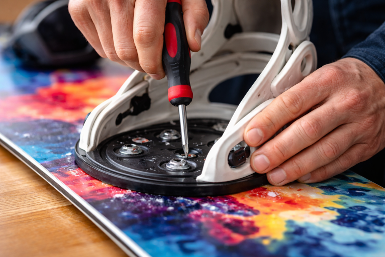 using a screwdriver to remove mounting hardware and bindings from a snowboard for off-season storage.